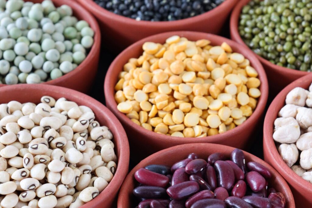 Full frame image of group of seven, orange-brown dishes filled with pulses, peas and beans, black (beluga) lentils, split yellow lentils, green peas, Mung beans, red kidney beans, black eyed peas, split red lentils, dried chickpeas, elevated view
